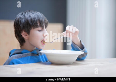 Boy eating le déjeuner de bol à table de cuisine Banque D'Images