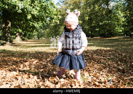Enfant de sexe féminin d'une façon incertaine entre les feuilles d'automne dans le parc Banque D'Images
