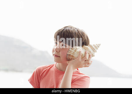 Boy holding seashell à oreille, Kraalbaai, Afrique du Sud Banque D'Images