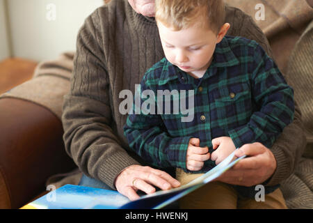 Garçon assis sur les genoux de grand-père reading book Banque D'Images