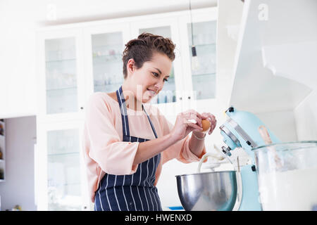 Jeune femme cracking oeuf dans un bol mélangeur alimentaire au comptoir de la cuisine Banque D'Images