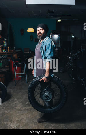 Portrait d'homme mûr, dans le garage, pneu moto holding Banque D'Images