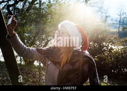 Jeune femme portant, à l'extérieur, wearing christmas hat, en tenant avec smartphone selfies Banque D'Images