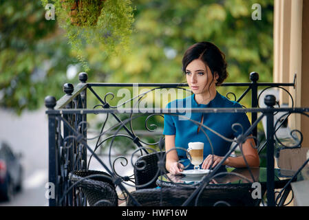 Jolie fille en robe élégante classique assis sur la terrasse de l'été à boire du café café Banque D'Images