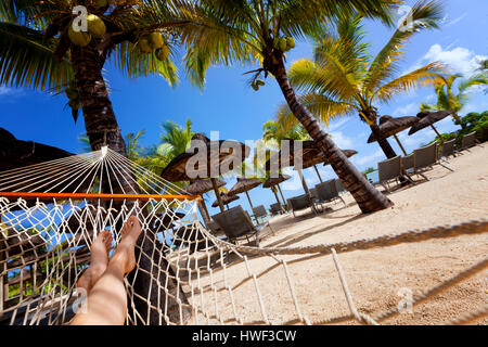 Sur Relaxig hamac sur la plage tropicale avec toiture en chaume en feuille de palmier de parasols et palmiers dans l'arrière-plan Banque D'Images