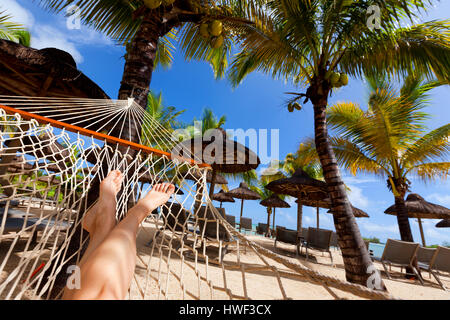 Sur Relaxig hamac sur la plage tropicale avec toiture en chaume en feuille de palmier de parasols et palmiers dans l'arrière-plan Banque D'Images