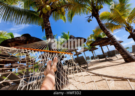 Sur Relaxig hamac sur la plage tropicale avec toiture en chaume en feuille de palmier de parasols et palmiers dans l'arrière-plan Banque D'Images