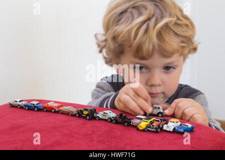 QUEENSTOWN, AFRIQUE DU SUD - 17 MAI 2015 - petite blonde boy playing with toy cars vintage sur le velours rouge fauteuil pouf - Se concentrer sur ses mains et des petites voitures Banque D'Images