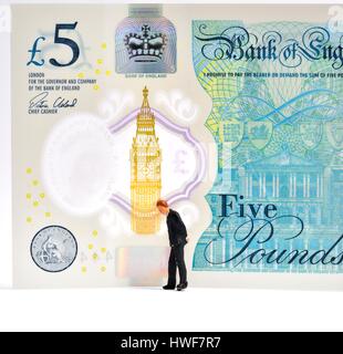 Figurine miniature business man standing in front of a 5 pound note. Banque D'Images