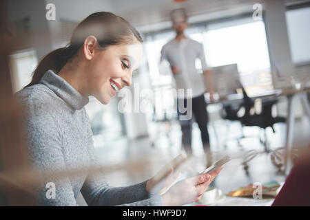 Smiling woman text messaging sur le travail Banque D'Images