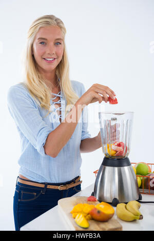 Portrait of smiling woman preparing smoothie against white background Banque D'Images