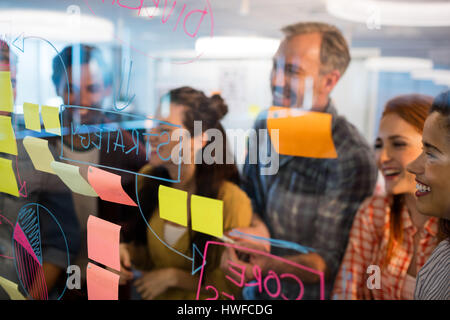 Creative Business team looking at sticky notes on glass window in office Banque D'Images