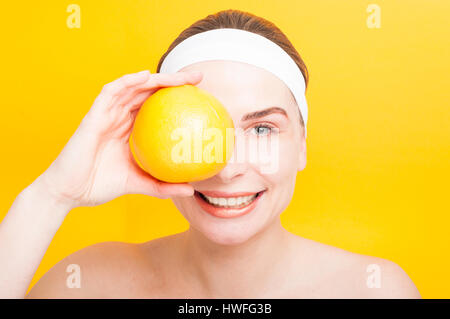 Portrait of woman holding big pamplemousses en face de son oeil isolé sur fond jaune Banque D'Images