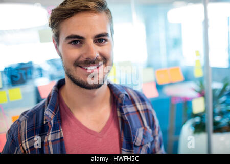 Portrait of smiling man standing contre les notes sur le mur de verre in office Banque D'Images