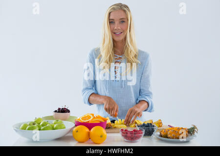 Portrait of smiling woman cutting fruits sur la planche à hacher against white background Banque D'Images