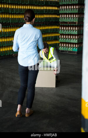 Vue arrière de la manager à la recherche de travailleur homme travaillant au warehouse Banque D'Images