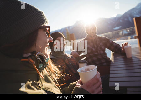 Amis skieurs en interaction les uns avec les autres tout en ayant des tasse de café dans station de ski Banque D'Images