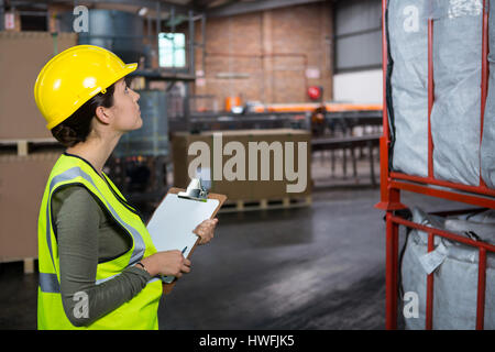 Vue latérale du travailleur féminin confiant l'examen de produits de warehouse Banque D'Images