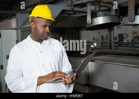 Travailleur homme sérieux portant manteau de laboratoire lors de l'utilisation d'ordinateur portable en usine jus Banque D'Images