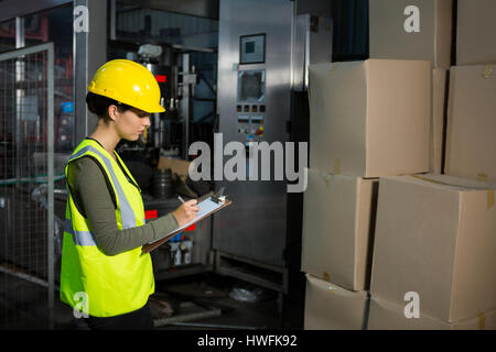 Vue latérale du travailleur féminin writing on clipboard in warehouse Banque D'Images