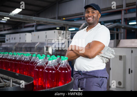 Portrait of male worker with arms crossed standing by bouteilles sur la ligne de production en usine Banque D'Images