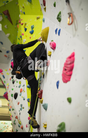 L'homme pratiquant l'Escalade sur mur d'escalade artificiel in gym Banque D'Images
