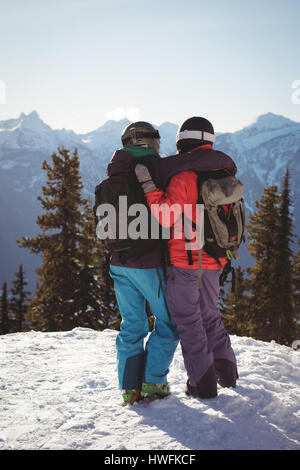 Vue arrière de deux skieurs debout avec bras autour de sur la montagne couverte de neige Banque D'Images