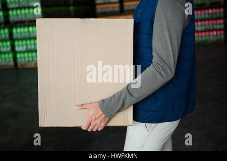 Mid section of worker carrying cardboard box in warehouse Banque D'Images