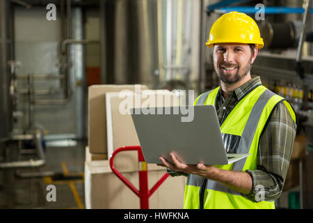 Portrait of smiling male worker using laptop in distribution warehouse Banque D'Images