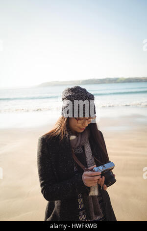 Femme regarder des photos sur un appareil photo numérique à la plage pendant la journée Banque D'Images