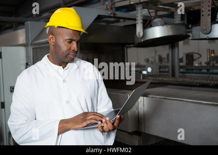 Travailleur homme sérieux portant manteau de laboratoire lors de l'utilisation d'ordinateur portable en usine jus Banque D'Images