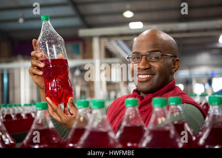 Portrait of smiling travailleur homme montrant jus bouteille en usine Banque D'Images