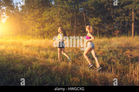 Les jeunes filles sportives fonctionnant sur un champ près de l'arbre au coucher du soleil en été. Athlète d'exécution sur l'off road dans la soirée. Femme active. Sport et guérir Banque D'Images