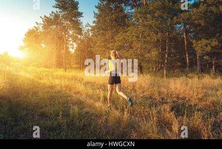 Jeune fille sportive s'exécutant sur un champ près de l'arbre au coucher du soleil en été. Athlète d'exécution sur l'off road dans la soirée. Femme active. Le sport et la santé. Banque D'Images