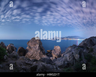 De hautes roches majestueuses et des pierres de lune rougeoyant à la mer. Nuit fantastique paysage panoramique avec des montagnes, les lumières de la ville, ciel étoilé avec le cloud Banque D'Images