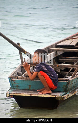 Un petit garçon prie tout en s'accroupissant sur la fin d'un bateau dans le village de Makyone Galet, Lampi, Parc national marin de l'archipel de Myeik, Myanmar Banque D'Images