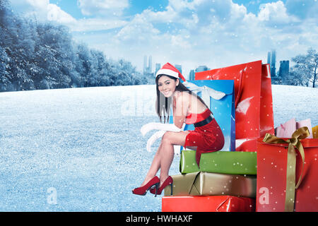 Young Asian Woman in santa costume s'asseoir sur la boîte-cadeau avec arrière-plan hiver Banque D'Images