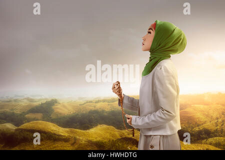 Jeune femme musulmane holding prayer beads standing on mountain Banque D'Images