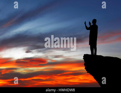 Silhouette de musulman, homme debout sur le haut de falaise. En priant et en cherchant à le ciel Banque D'Images