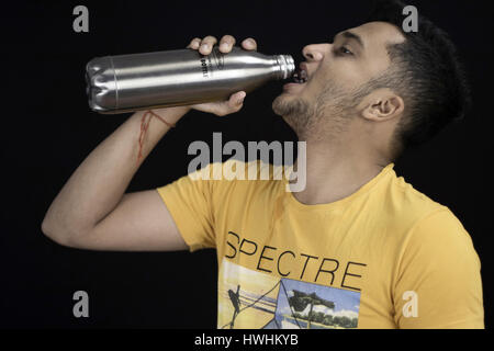 L'eau potable l'homme à partir d'une bouteille en acier avec la tête relevée et fond noir Banque D'Images