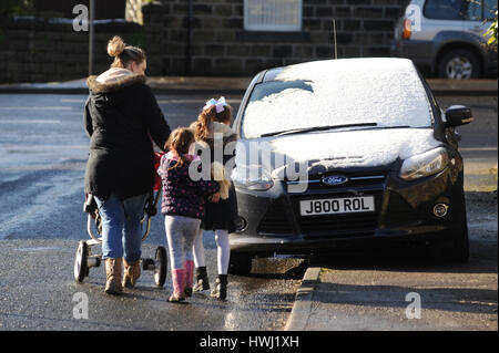 Une femme marche dangereusement ses enfants autour d'une voiture qui est garée sur le trottoir. Banque D'Images