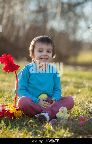 Adorable garçon dans le parc, s'amusant avec les oeufs colorés pour Pâques, printemps Banque D'Images