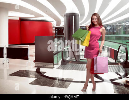 Smiling young asian woman with shopping bags sur fond mall Banque D'Images