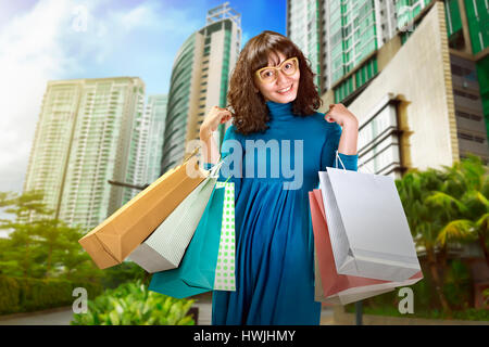 Femme Asiatique se trouve près de la Mall. Elle porte robe et lunettes, et elle détient les sacs dans sa main Banque D'Images