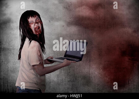 Zombie femelle Creepy tapant avec ordinateur portable plus grunge background Banque D'Images