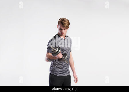 Bel homme fitness hipster dans Grey T-shirt l'élaboration avec haltère. Studio shot sur fond gris. Banque D'Images