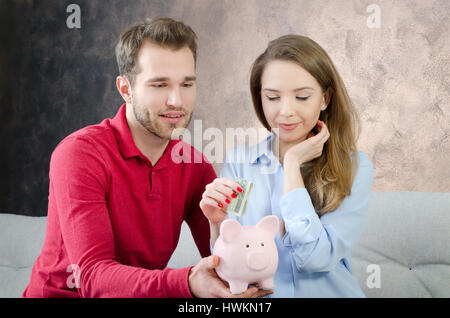 Jeune couple enregistre en tirelire. Les économies de l'argent couple piggybank accueil concept coût mariage budget Banque D'Images