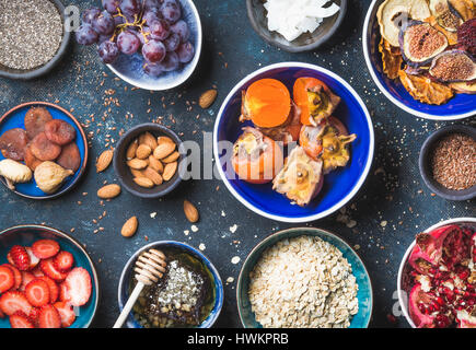 Ingrédients dans des bols pour petit-déjeuner sain sur fond bleu foncé, vue du dessus. Fruits frais et secs, graines de chia, gruau, noix, miel. L'alimentation, Banque D'Images
