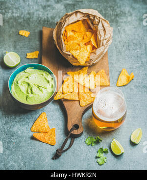 Croustilles de maïs mexicain, sauce guacamole frais et un verre de bière sur sol en bois servant au conseil d'arrière-plan du tableau de béton gris, vue du dessus, selective focus Banque D'Images