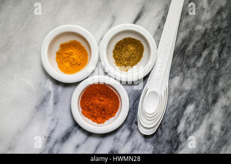 Haut en bas de l'image sélection d'épices colorés dans de petits plats blanc avec ensemble de cuillères à mesurer en plastique sur en arrière-plan. Le curcuma, le cumin et pa Banque D'Images